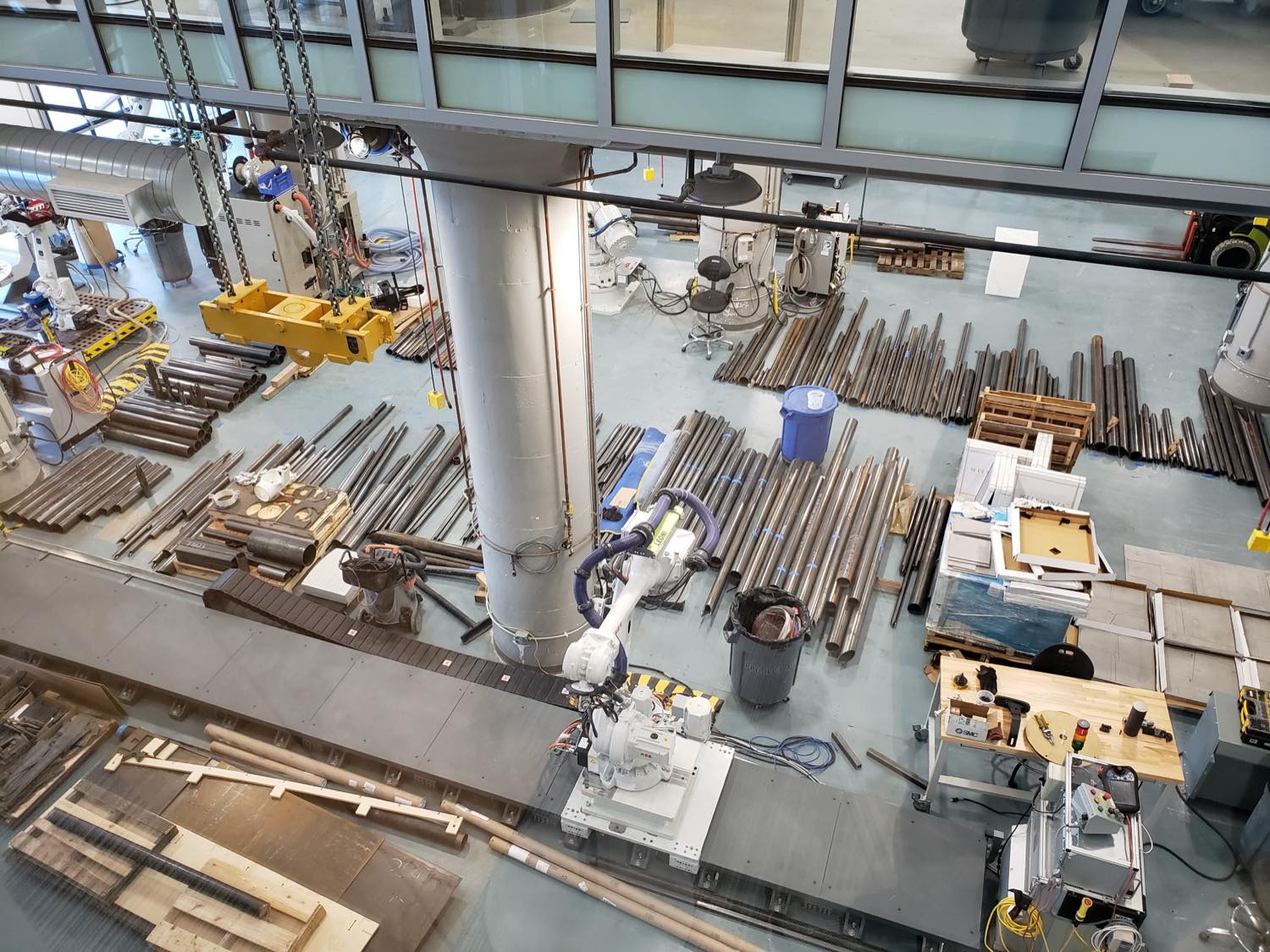 Overhead view of the Boston shop floor covered with hundreds of cut steel tubes, with an ABB robot arm on a linear track among them