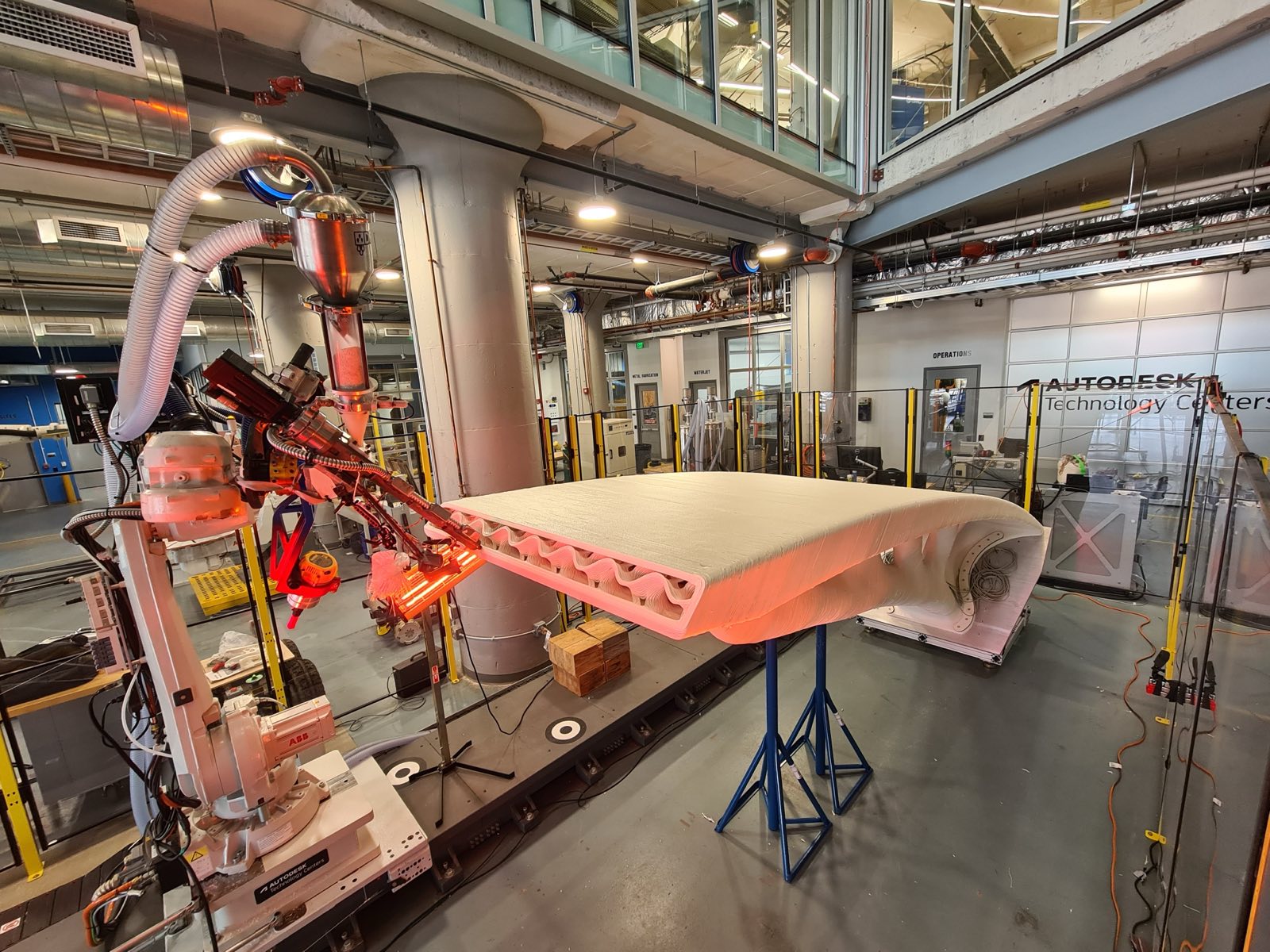 The robot arm extruding the curved deck surface of the bridge, lit orange by the heated nozzle