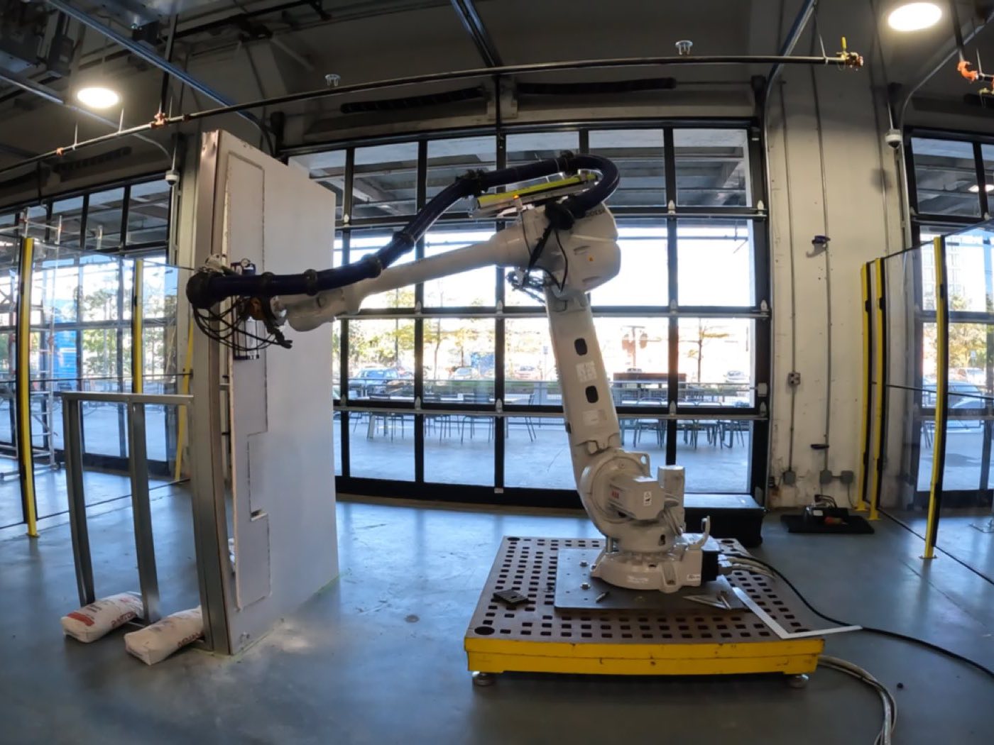 An ABB robot arm on a mobile base working against a full-height drywall panel in the robotics lab