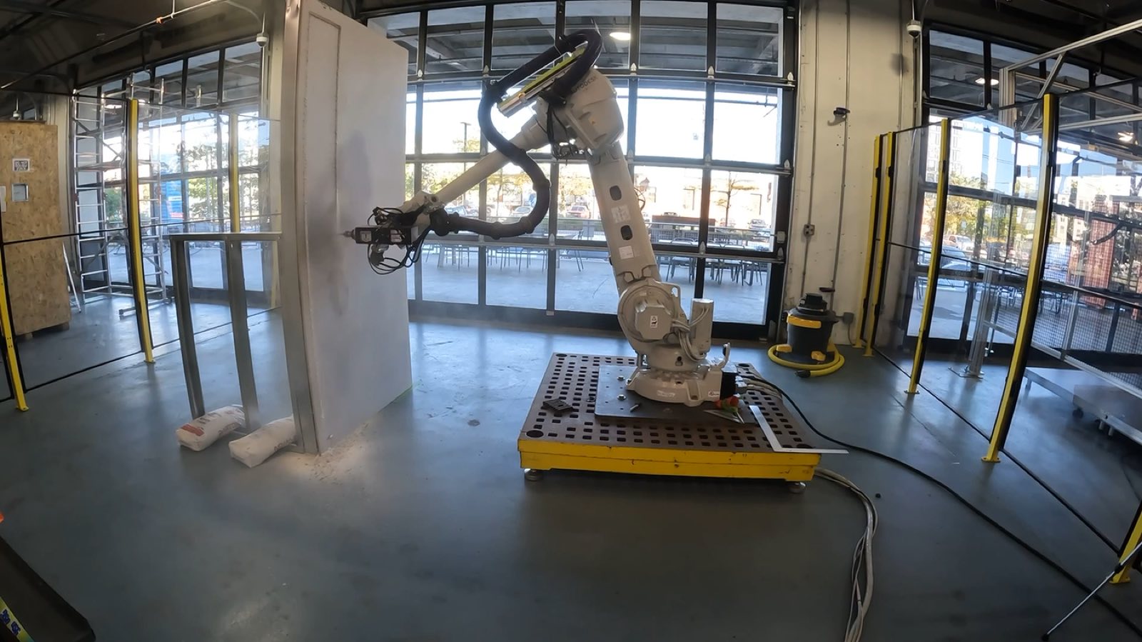 Wide view of the robot cell in the shop with a drywall panel mounted vertically on a stud frame