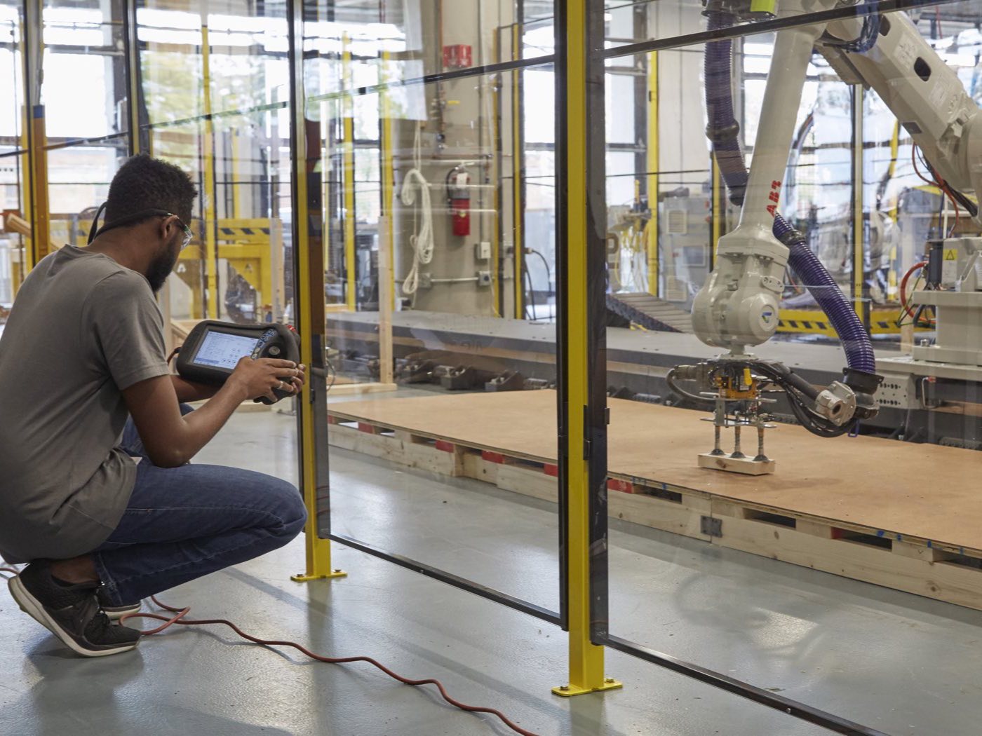 A technician crouching with a teach pendant, programming a large ABB robot on a linear rail behind safety fencing