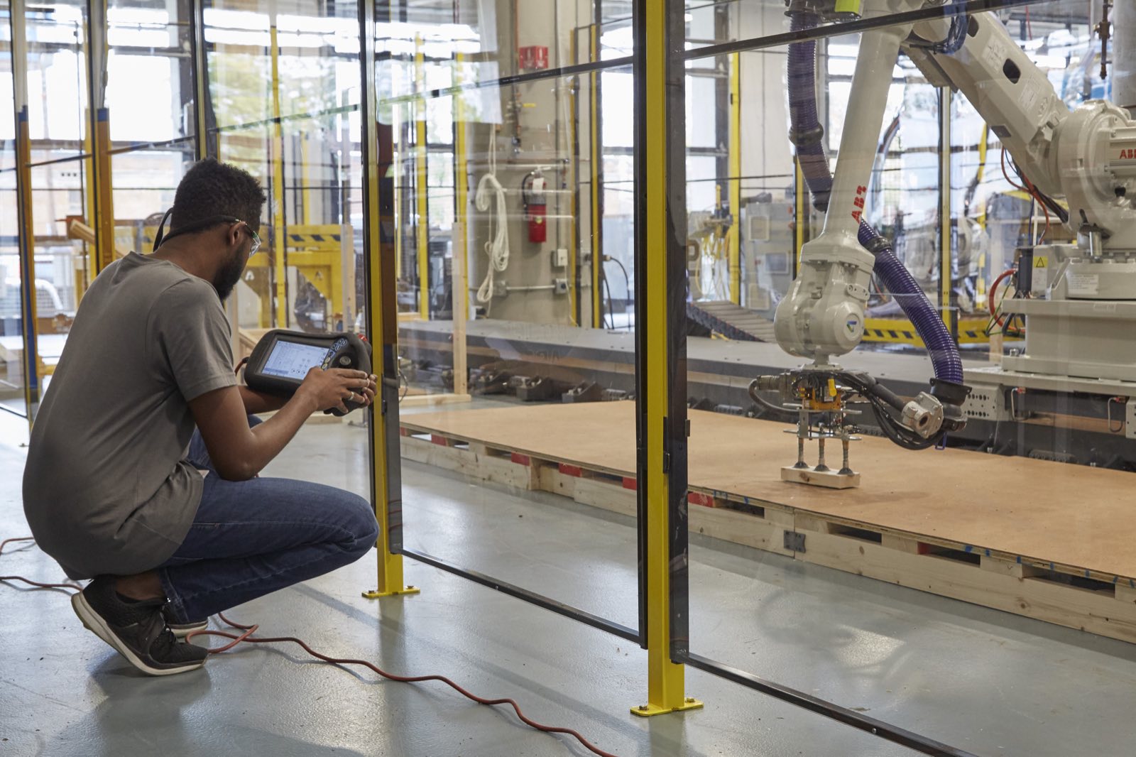 A technician crouching with a teach pendant, programming a large ABB robot on a linear rail behind safety fencing