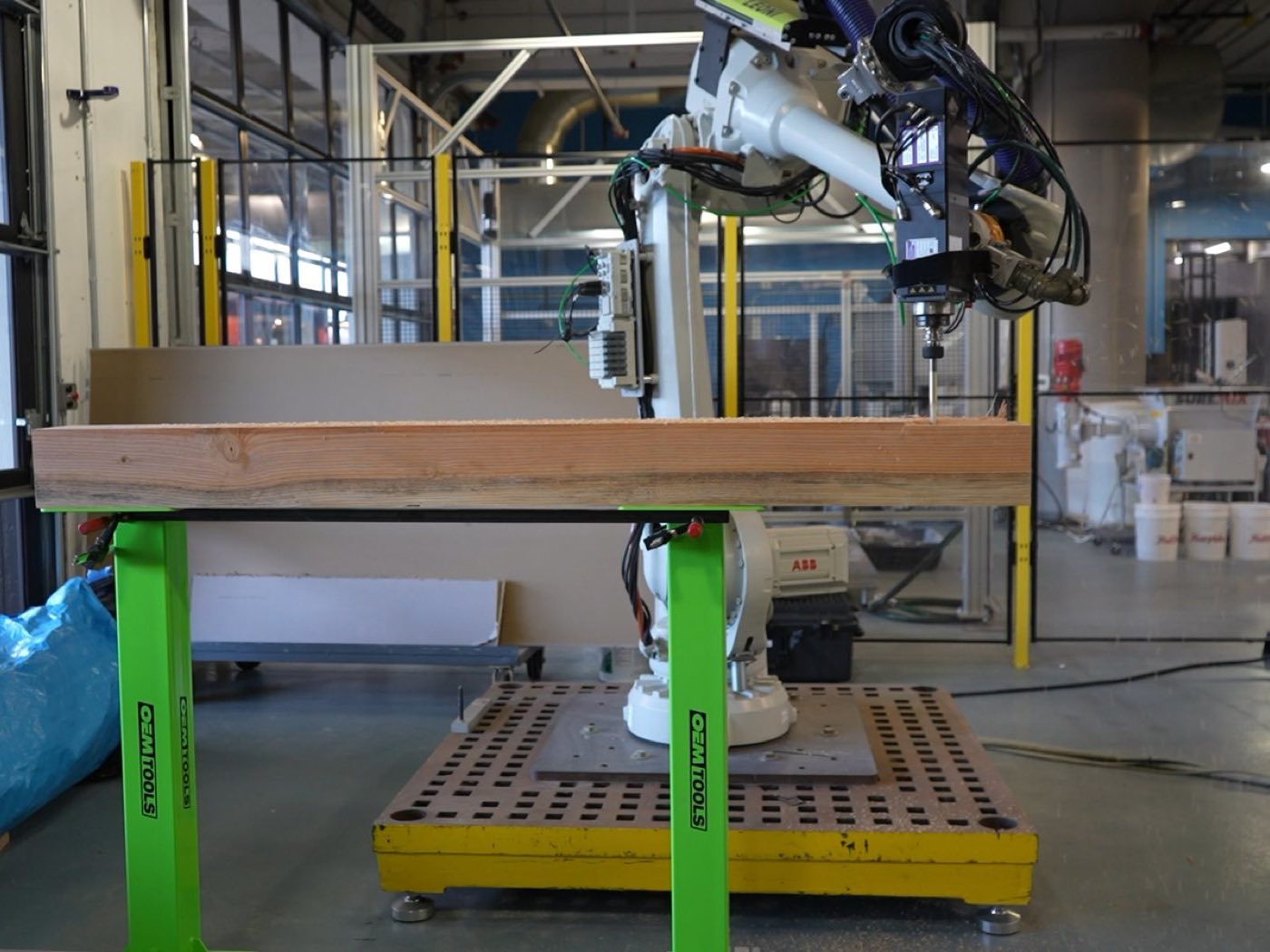 An ABB robot arm with a spindle end effector milling a joint into a large timber truss cross member clamped on green stands