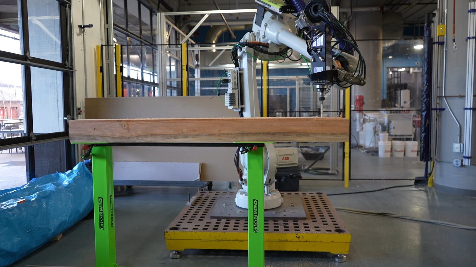An ABB robot arm with a spindle end effector milling a joint into a large timber truss cross member clamped on green stands